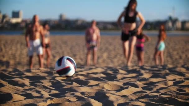 Um grupo de amigos joga vôlei de praia, uma menina morena esbelta corre atrás da bola — Vídeo de Stock