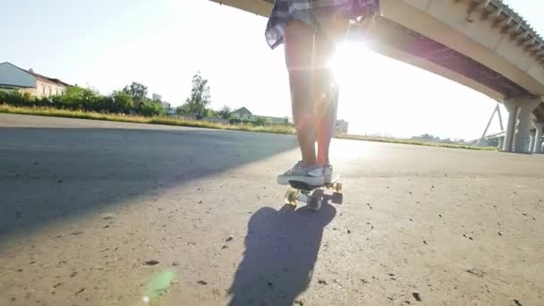 Красивая девушка ездит на скейтборде, в рамке стройные ноги, солнечные лучи — стоковое видео