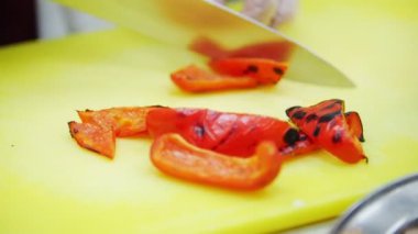 Bir aşçı adet közlenmiş biber sarı tahtada keser.