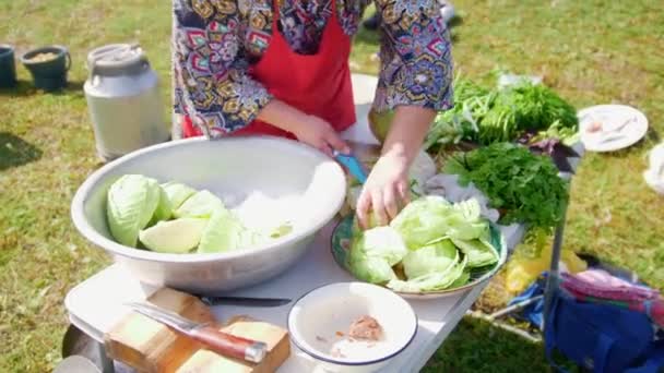 Жінка ріже капусту під час походу, на столі багато зелені — стокове відео