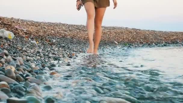 Молодая девушка идет вдоль скалистого берега, в рамке красивых ног — стоковое видео