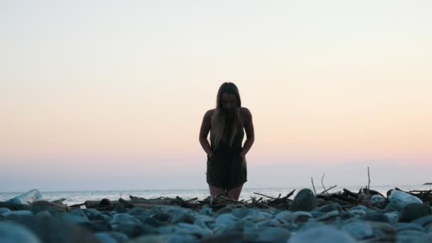 Hermosa joven camina en una playa rocosa y va a la cámara — Vídeos de Stock