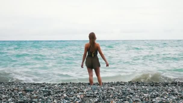 Niña caminando por la costa rocosa del mar. Hay olas. Las chicas pelo largo es soplado por el viento . — Vídeo de stock