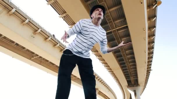 Un joven Popper con sombrero y una camiseta a rayas bailando bajo el puente en verano, muestra estilo libre — Vídeos de Stock