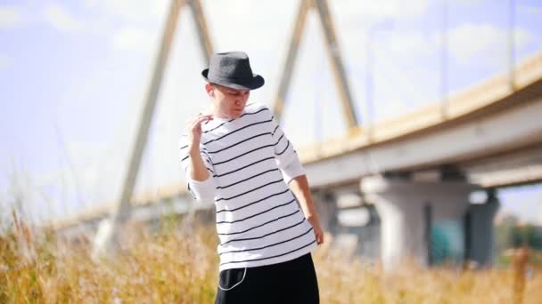 Joven bailarina popper en un sombrero está bailando intensamente en la calle contra el puente en un día soleado de verano — Vídeos de Stock
