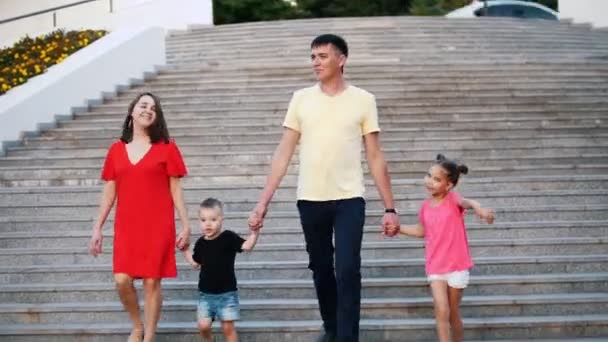 Unga lycklig familj: far, mor, dotter och son i parken. De går ner trappan och prata. — Stockvideo