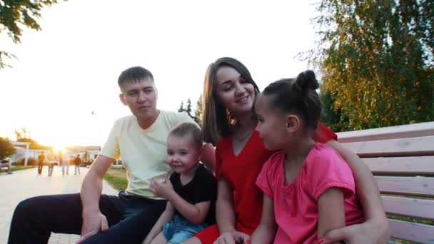 Familia sentada en el parque. Papá, mamá, hermano y hermana están hablando. Día soleado de verano . — Vídeo de stock