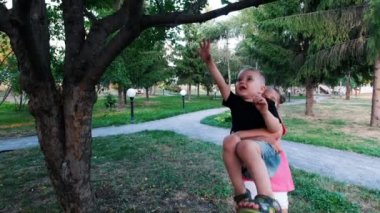 Küçük kız küçük kardeşini ağaç dalı ulaşmak için onun kollarında yükseltir. Çocuk uzanıyor ve iki eliyle tutan.