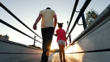 Kızları elini tutan, onunla parkta bir ahşap platform üzerinde günbatımında yürüyen bir adam. Anne ve baba kızı ile yürüyüş oğlu.