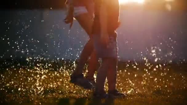 Los niños saltan sobre los charcos en la hierba, crean un hermoso spray que brilla al sol. Momento mágico . — Vídeos de Stock