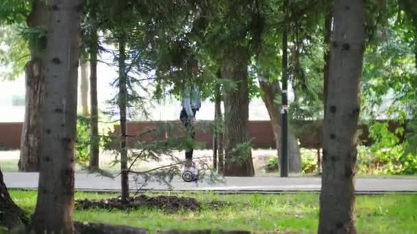 Fille conduit devant la caméra sur un gyroscope dans le parc parmi les arbres — Video