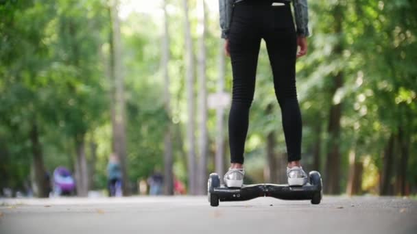 Hermosa chica delgada con el pelo largo monta un giroscopio en el parque, vista trasera — Vídeos de Stock