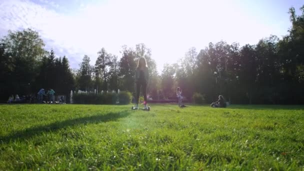 年轻漂亮的女孩骑着陀螺在草地上。夏天的日子。太阳的眩光. — 图库视频影像