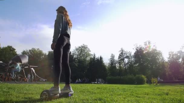 Jeune fille attrayante chevauchant un gyroscope sur l'herbe dans le parc. Jour d'été. A côté du reste de la population . — Video