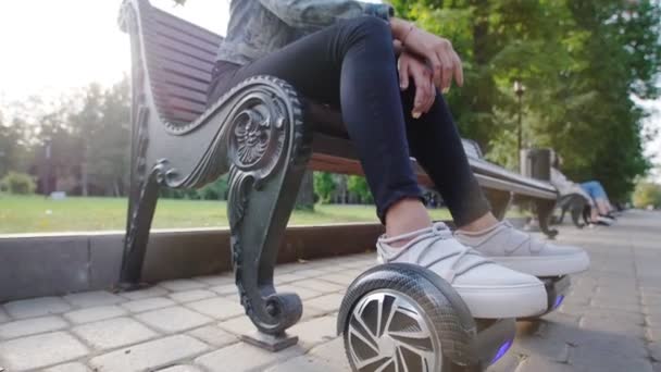 Meisje zorgvuldig zittend op het bankje in het Park. Haar voeten zijn op de gyro. Zomer. — Stockvideo