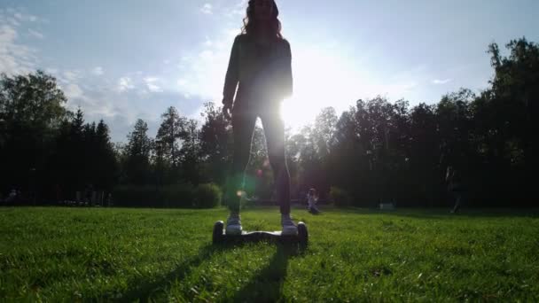 Ein Mädchen mit einer schönen schlanken Figur, das im Sommer auf dem Gras im Park auf einem Kreisel reitet. die Sonne scheint. — Stockvideo