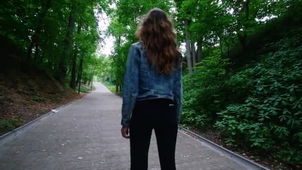 Junge Frau mit schlanker Figur, schönen Locken, die auf einem Kreisel im Park reiten. In der Hosentasche steckt das Telefon. — Stockvideo