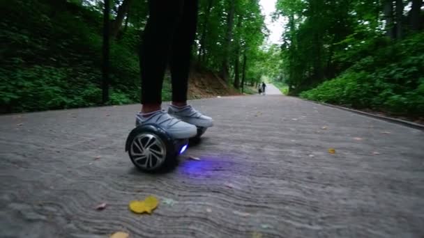 In the frame of womens legs in sneakers. Girl riding a gyro in the forest in the park. Slow Motion. — Stock Video