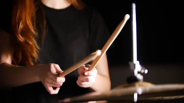 Рудоволоса дівчина грає на музичних барабанах у темній студії. Руки, барабанні палички . — стокове фото