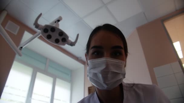 Una dentista donna in maschera dirige la luce della lampada verso la fotocamera. Lo studio dentistico . — Video Stock