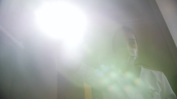 Mulher dentista endireita a lâmpada e olha para a câmera com uma ferramenta na mão . — Vídeo de Stock