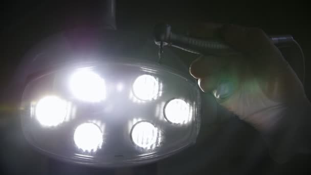 A mão do dentista segura o irrigador na frente da câmera no fundo da lâmpada e liga-o — Vídeo de Stock