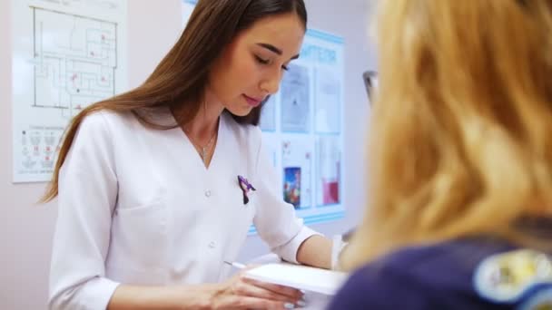 Mujer dentista lee el libro médico de pacientes de una mujer que se sienta enfrente. Visita al dentista — Vídeos de Stock