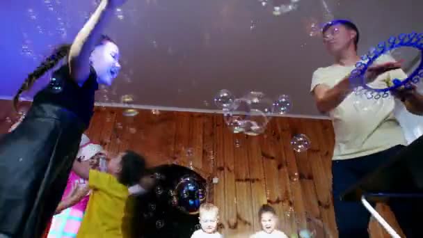 L'animatore ha organizzato uno spettacolo di bolle di sapone per bambini. I bambini saltano e ballano sotto molte bolle . — Video Stock