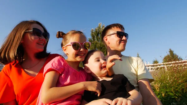 Молодая счастливая семья, сидящая в парке в солнечный летний день в солнцезащитных очках — стоковое фото