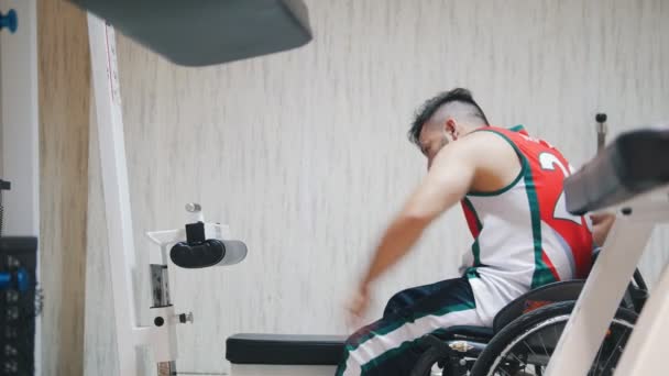 Инвалид встает с инвалидной коляски, делает упражнения и тяжело дышит во время тренировки в спортзале — стоковое видео