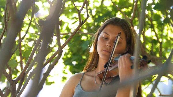 Молодая девушка играет на старинной скрипке на природе — стоковое фото