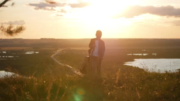 Pojke med en gitarr i en blå jacka går från solnedgången — Stockvideo