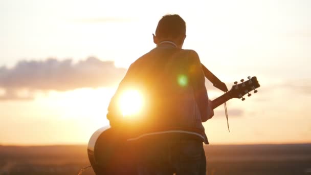 Chłopiec w okrągłe okulary, gra na gitarze w dziedzinie w zachód słońca — Wideo stockowe