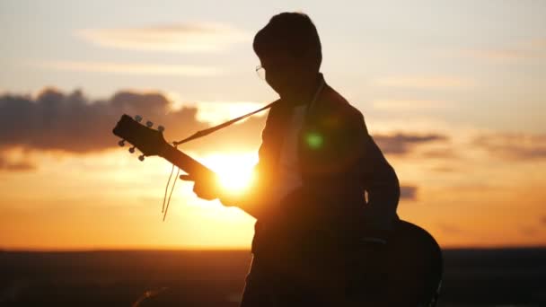 Niño en gafas redondas tocando la guitarra en el campo al atardecer — Vídeos de Stock