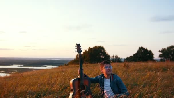 Boy standing with wooden guitar in the field — Stock Video