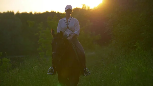 Jovem cavaleiro com um boné de beisebol branco montando um cavalo marrom — Fotografia de Stock