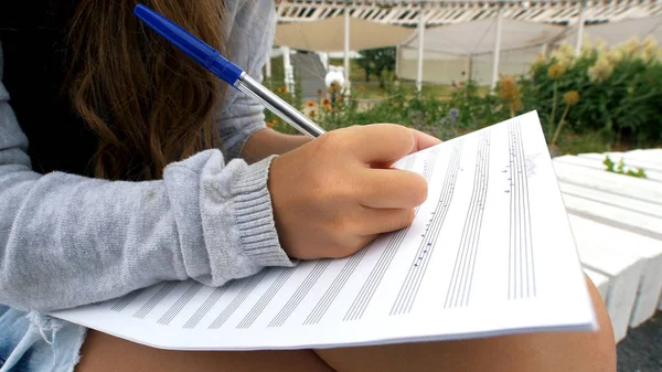 Девушка пишет музыку на нотах, сидя в парке — стоковое фото
