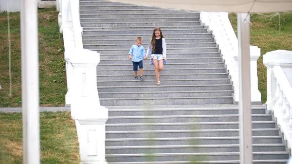 Маленькая блондинка и еще молодой блондин прогуливаются по парку и спускаются по лестнице. — стоковое фото