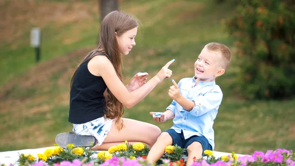 Little blonde girl and her younger friend are playing with paint in the park — Stock Photo, Image