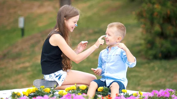 Little blonde girl and her younger friend are playing with paint in the park — Stock Photo, Image