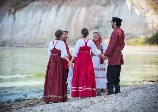 Группа людей в русских народных костюмах танцует в красивом пейзаже, на переднем плане аккордеон — стоковое фото
