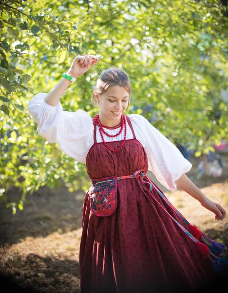 Красивая молодая девушка в русском народном сарае танцует на фоне зеленых деревьев — стоковое фото