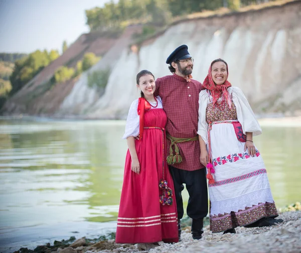 Bir adam ve iki kadın Rus ulusal kostümleri muhteşem bir manzara arka plan üzerinde kamera için poz — Stok fotoğraf