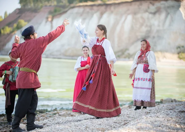 Молодежь в национальных костюмах России танцует народные танцы, играет на аккордеоне — стоковое фото