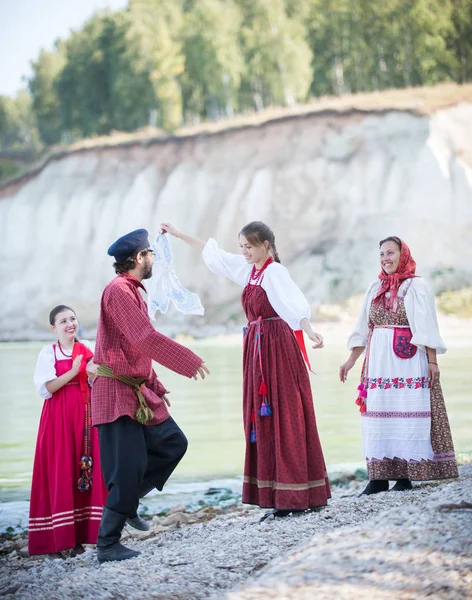 Молодежь в национальных костюмах России танцует народные танцы на фоне удивительного ландшафта — стоковое фото