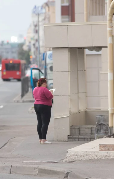 Plus-size jonge vrouw staat terug naar de camera en schrijft in een notitieblok op de straat — Stockfoto
