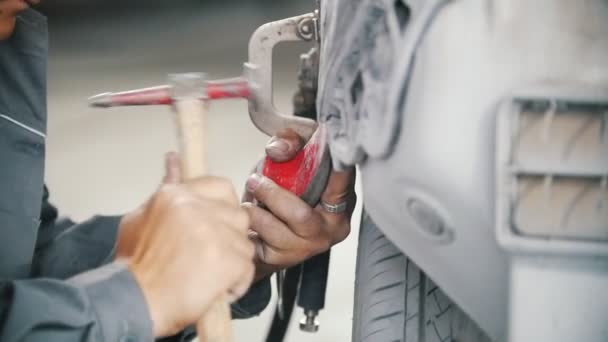 Mens handen reparatie een auto met een hamer in een auto reparatiewerkplaats — Stockvideo
