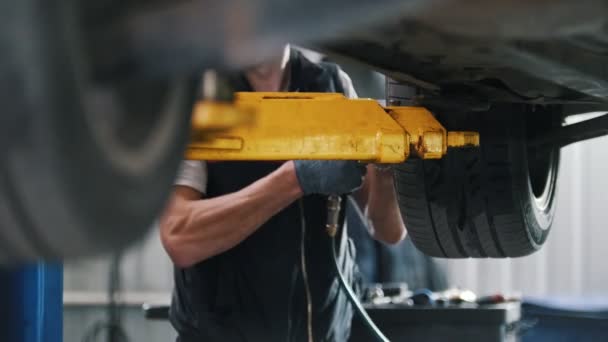 Mechaniker schraubt das Rad in einem Auto, das in der Werkstatt auf einen Kran gehoben wird — Stockvideo