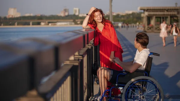 Girl With Red Hair And Guy On A Wheelchair Talking On The Waterfront On A Summer Evening — Stock Photo, Image
