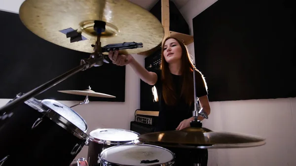 Young red-haired girl working behind a drum set in a dark studio — Stock Photo, Image